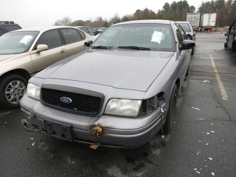 Gray Ford Crown Victoria with damaged front bumper and missing headlight, parked in a lot