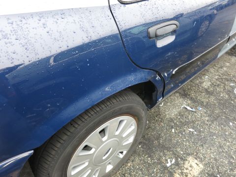 1991 Ford LTD Crown Victoria - Side view of a blue 1991 Ford Crown Victoria LTD, showing the rear wheel well and a damaged door.