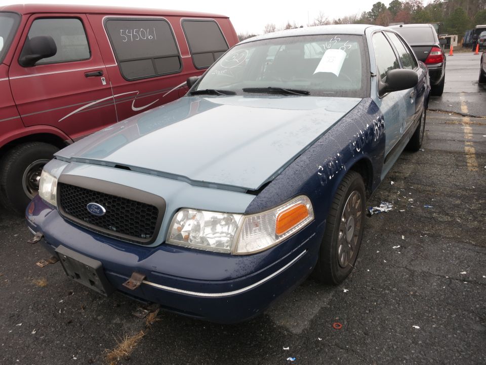 Ford Crown Victoria with a light blue hood and dark blue fenders. A red van is parked to its left