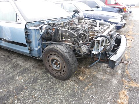1991 Ford LTD Crown Victoria - The front end of a light blue sedan is shown with its engine compartment exposed, revealing wiring and mechanical components.