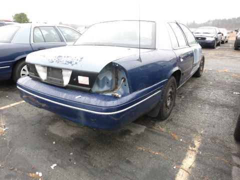 1991 Ford LTD Crown Victoria - A blue Ford Crown Victoria is parked in a lot, showing damage to its rear and missing a tail light.