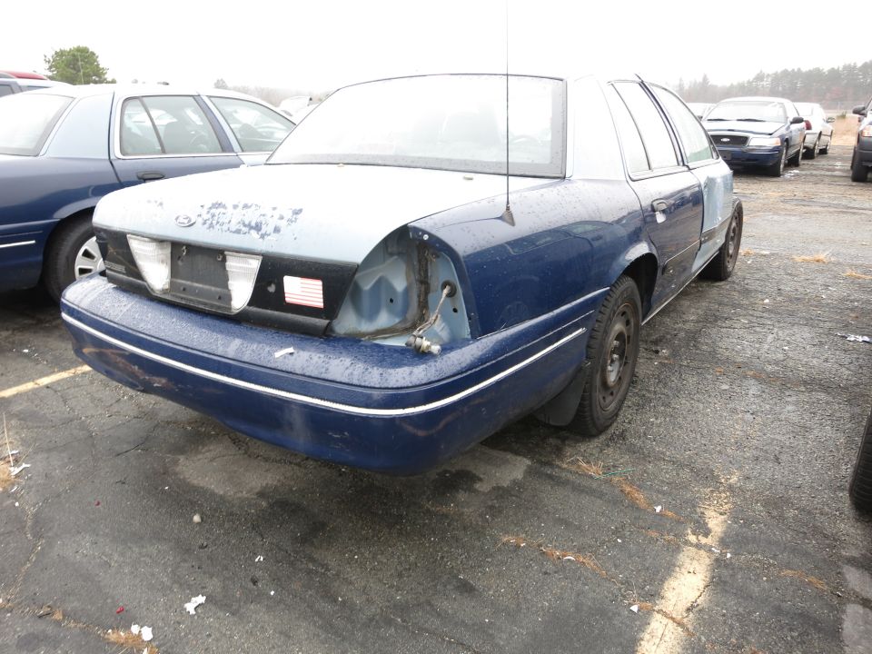 Blue Ford Crown Victoria, rear view, missing tail light. Another blue Crown Victoria is next to it