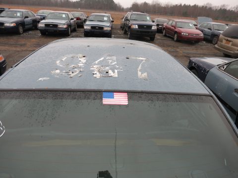 1991 Ford LTD Crown Victoria - A car's roof displays the numbers '947' with peeling paint and an American flag sticker, with other vehicles visible in the background.