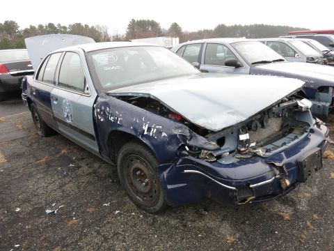 1991 Ford LTD Crown Victoria - A wrecked Ford Crown Victoria sits in a junkyard with its hood up and front end severely damaged.