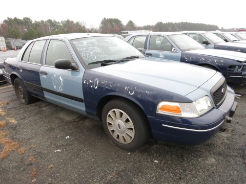 1991 Ford LTD Crown Victoria - A two-tone police car sits in a lot with other vehicles, showing markings on its hood and door.