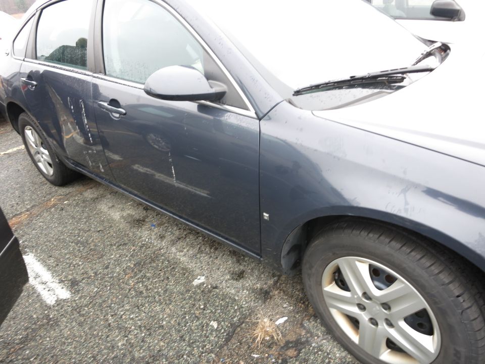 Dark blue sedan, driver's side door has significant damage and white scuff marks. Front wheel and fender visible
