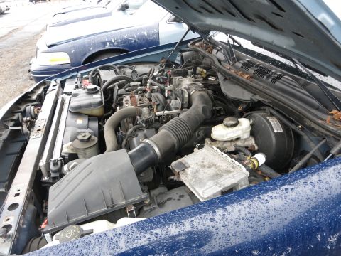 1991 Ford LTD Crown Victoria - The engine bay of a blue car is visible, with another similar vehicle parked behind it.