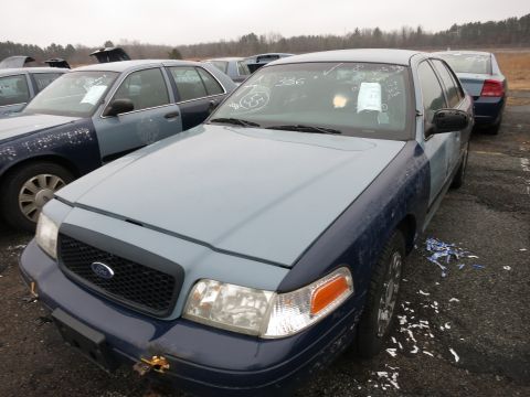 1991 Ford LTD Crown Victoria - A two-tone Ford Crown Victoria sits in a junkyard with other vehicles. Writing is visible on the windshield.
