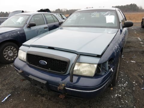 1991 Ford LTD Crown Victoria - A blue and gray Ford Crown Victoria sits in a junkyard, showing damage to its front end and hood.