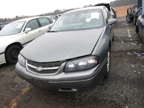 1991 Ford LTD Crown Victoria - A gray Chevrolet Impala sits in a junkyard with its hood open, parked next to other vehicles.