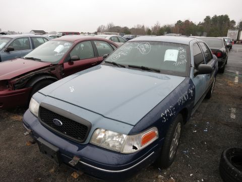 1991 Ford LTD Crown Victoria - A two-tone Ford Crown Victoria sits in a junkyard with other vehicles, its windshield marked with white writing.
