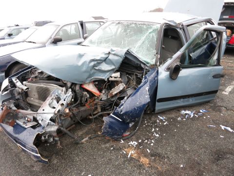 1991 Ford LTD Crown Victoria - A heavily damaged blue sedan sits on asphalt, with debris scattered around its front end.