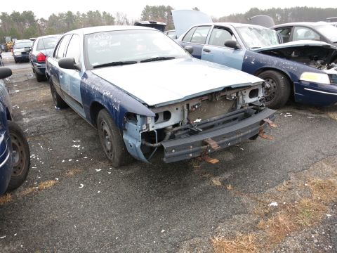 1991 Ford LTD Crown Victoria - A damaged Ford Crown Victoria sits in a junkyard, with other vehicles visible in the background.