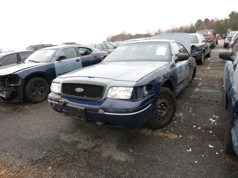 1991 Ford LTD Crown Victoria - A blue Ford Crown Victoria is parked in a junkyard with its headlights missing.