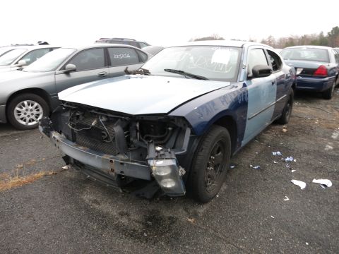 1991 Ford LTD Crown Victoria - A damaged Dodge Charger, formerly a police vehicle, sits in a junkyard with its front bumper and headlights removed.