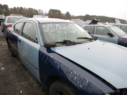 1991 Ford LTD Crown Victoria - A two-tone police car sits in a junkyard with other vehicles, showing 'POLICE' text on the fender and handwritten notes on the windshield.