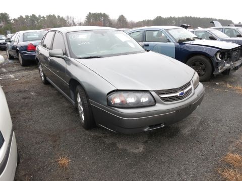 1991 Ford LTD Crown Victoria - A gray Chevrolet Impala is parked in a junkyard next to other vehicles.