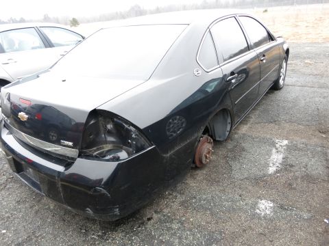 1991 Ford LTD Crown Victoria - A black sedan is seen from the rear, missing a wheel and with damage to its bumper and taillight assembly.