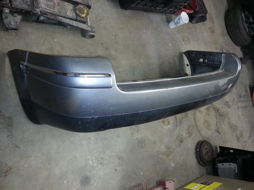 Car's rear bumper, gray with chrome trim, sitting on a concrete floor