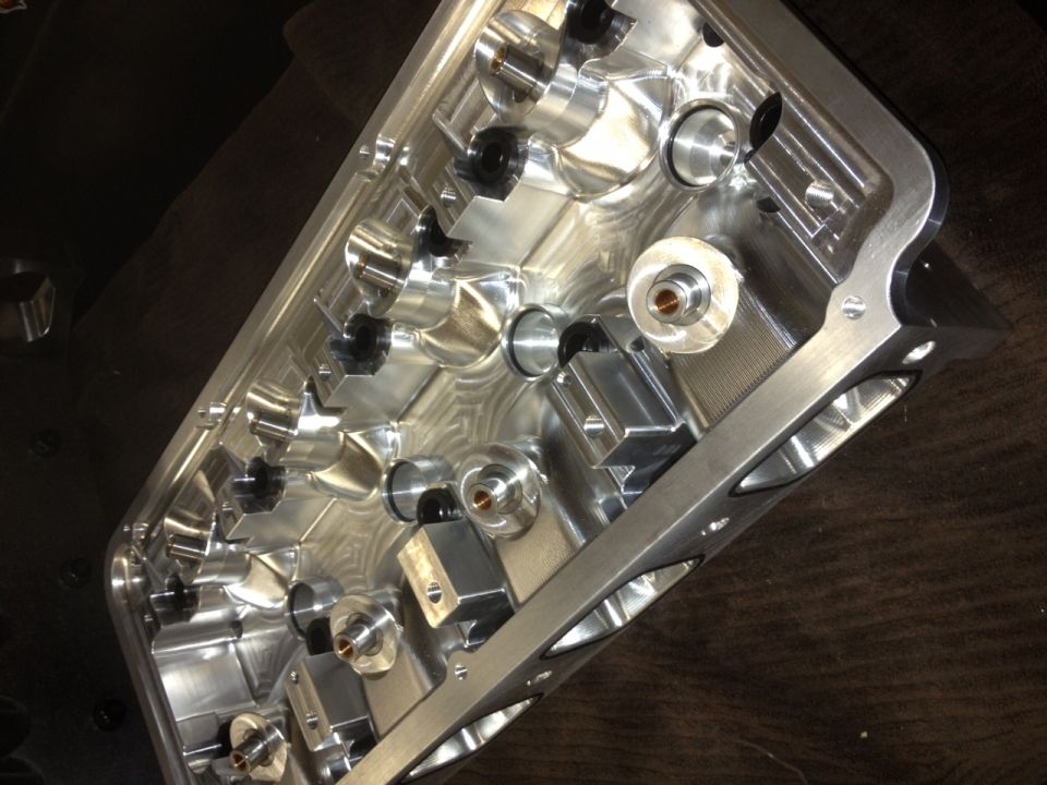 Close-up of a shiny, complex machined aluminum engine component with many ports and bolt holes