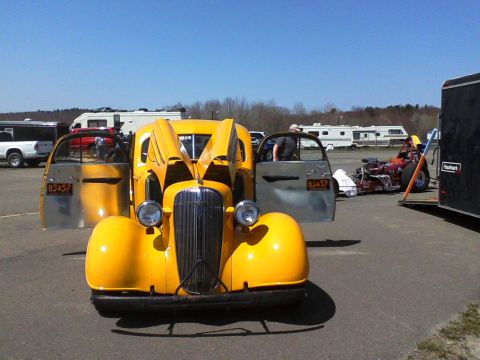 1935 Chevrolet new - A yellow 1936 Chevrolet Master Deluxe sedan is shown with its hood and doors open, parked in an outdoor lot with other vehicles and RVs.