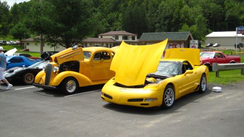 1935 Chevrolet new - Two yellow cars, a 1935 Chevrolet and a modern Corvette, are parked with their hoods open.