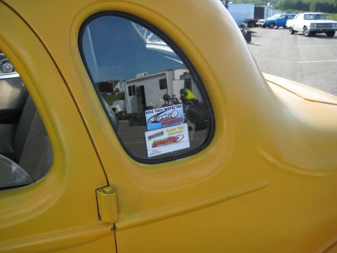 1935 Chevrolet new - A yellow coupe is parked outside with several stickers on its window, and other vehicles are visible in the background.