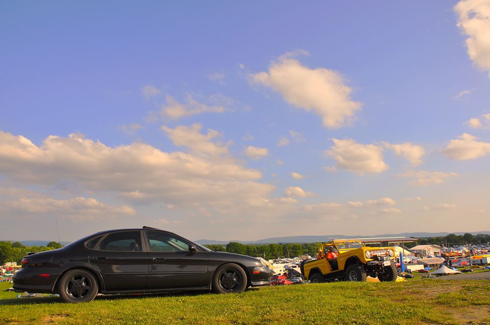 Black 1997 Ford Taurus sedan parked on grass with yellow off-road vehicle in background