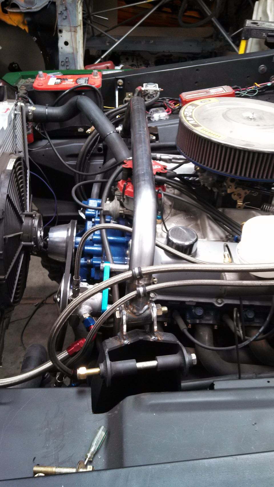 Engine bay showing custom exhaust pipe, air filter, radiator fan, and battery