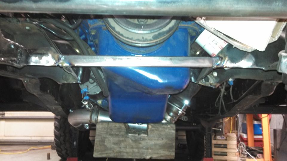 Underside view of a blue oil pan and engine components, with exhaust pipes and suspension visible