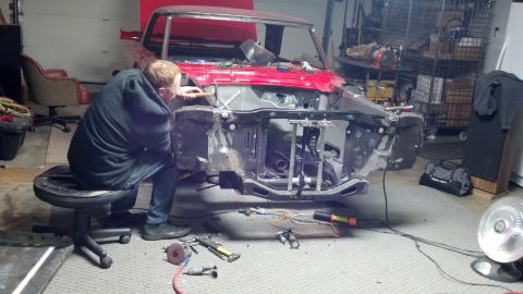 1964 Ford Fairlane - A person works on the front end of a red car in a garage.