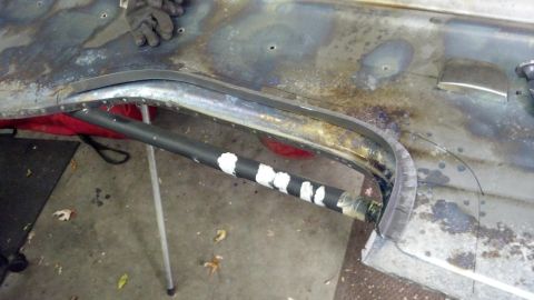 1964 Ford Fairlane - A close-up view shows a section of a car's bodywork, including a metal trim piece and a pipe with white markings.