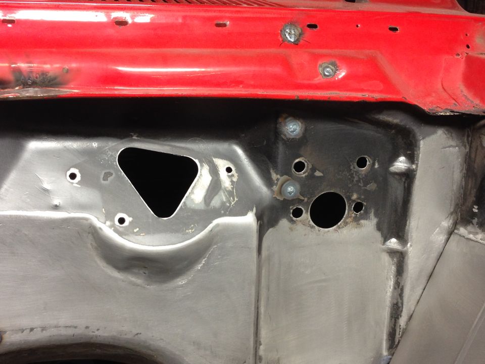 Close-up of a car's red-painted firewall with metal bracing and holes