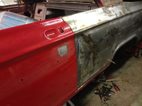 1964 Ford Fairlane - A car's side panel is undergoing repair, with one section painted red and the other showing bare metal and welding marks.