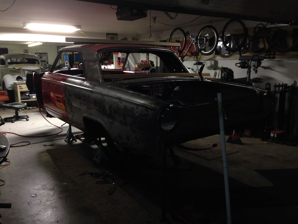 1964 Ford Fairlane body on jack stands in a garage, undergoing restoration. Another car is visible in the background