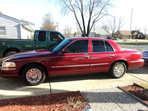 2004 Mercury Grand Marquis - Side profile of a red 2004 Mercury Grand Marquis parked next to a green pickup truck.