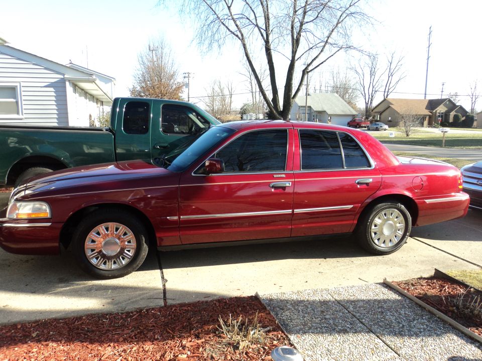 2004 Mercury Grand Marquis parked on a driveway, side view. Green pickup truck is to the left