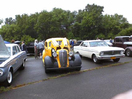 1935 Chevrolet new - A yellow hot rod with its hood open is parked at an outdoor car show.