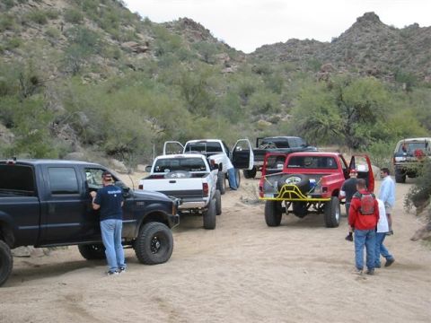 1994 Ford Bronco - A group of off-road vehicles are gathered in a desert area, with several people interacting near the trucks.