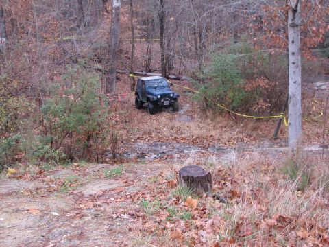 1979 Ford Bronco - A Jeep Wrangler navigates a wet, wooded trail with yellow caution tape visible.