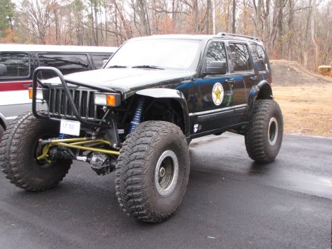 1979 Ford Bronco - Modified Jeep Grand Cherokee on large tires, a custom bumper and suspension. Another vehicle is parked nearby.