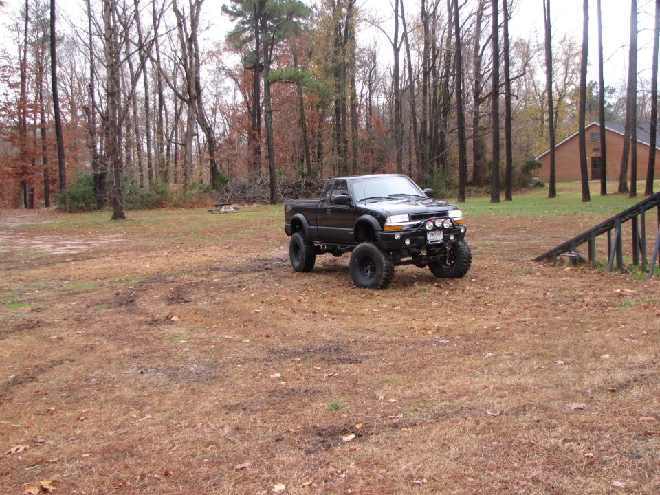 Lifted black pickup truck with large tires parked in a grassy, wooded area