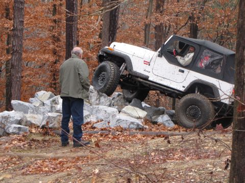 1979 Ford Bronco - A white Jeep Wrangler navigates a rocky obstacle course in a wooded area.