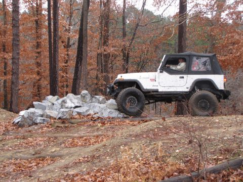 1979 Ford Bronco - A white Jeep Wrangler navigates a rocky obstacle on a wooded trail during autumn.
