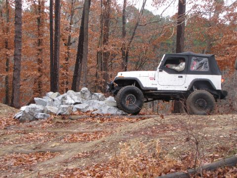 1979 Ford Bronco - A white Jeep Wrangler tackles a rocky obstacle on an off-road trail surrounded by autumn trees.