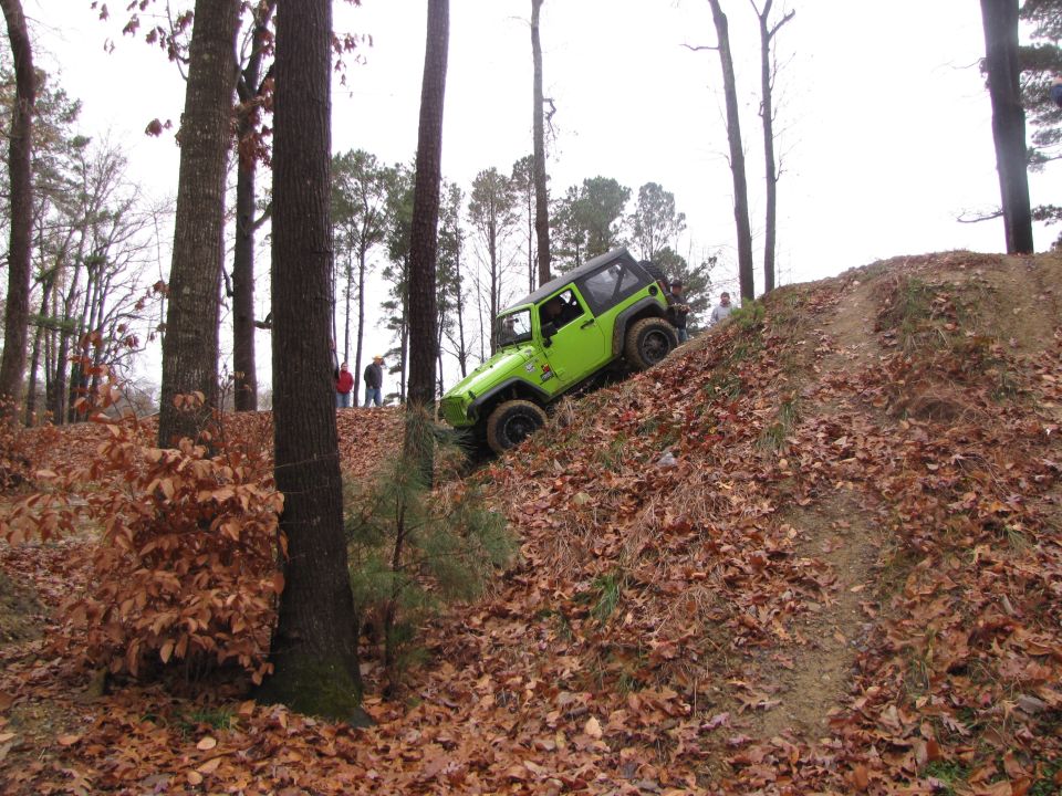 Green Jeep Wrangler driving up a leaf-covered hill in a wooded area