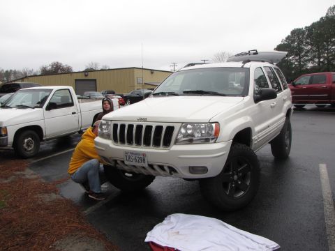 1979 Ford Bronco - A white Jeep Grand Cherokee is being worked on by two people, with a white pickup truck in the background.