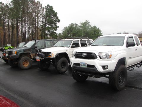 1979 Ford Bronco - Several modified off-road vehicles are parked in a line on a paved surface.