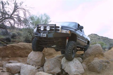 1994 Ford Bronco - This black pickup truck navigates a rocky trail, its off-road capabilities and aftermarket modifications. The grille design points to a 199…