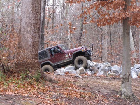 1979 Ford Bronco - Jeep Wrangler navigating a rocky obstacle on an off-road trail in a wooded area.